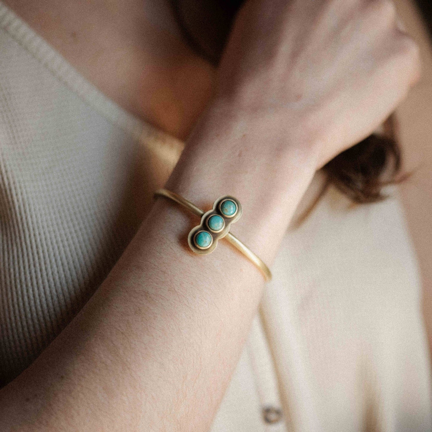 Gold bracelet with turquoise stones on a wrist against a neutral background