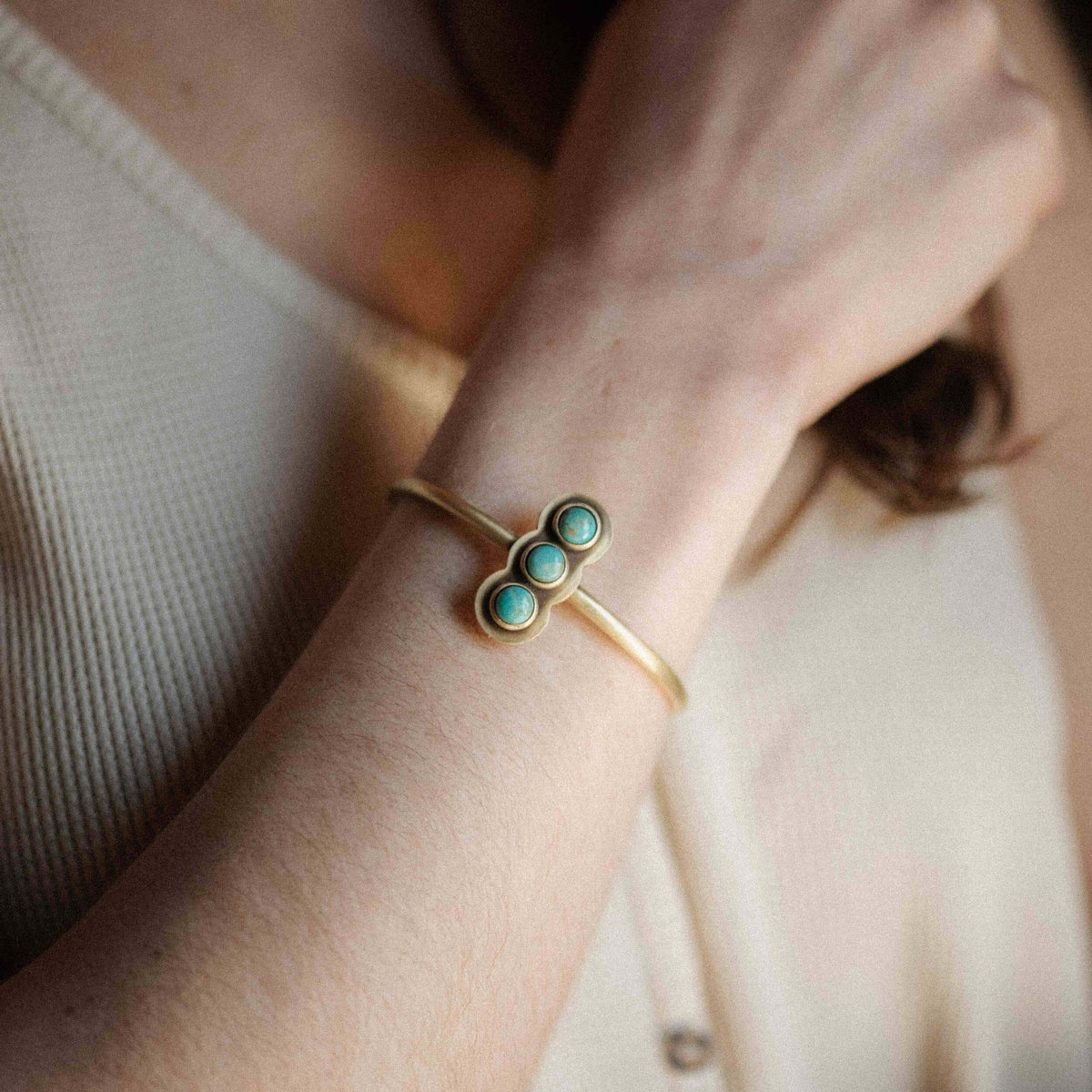 Gold bracelet with turquoise stones on a wrist against a neutral background