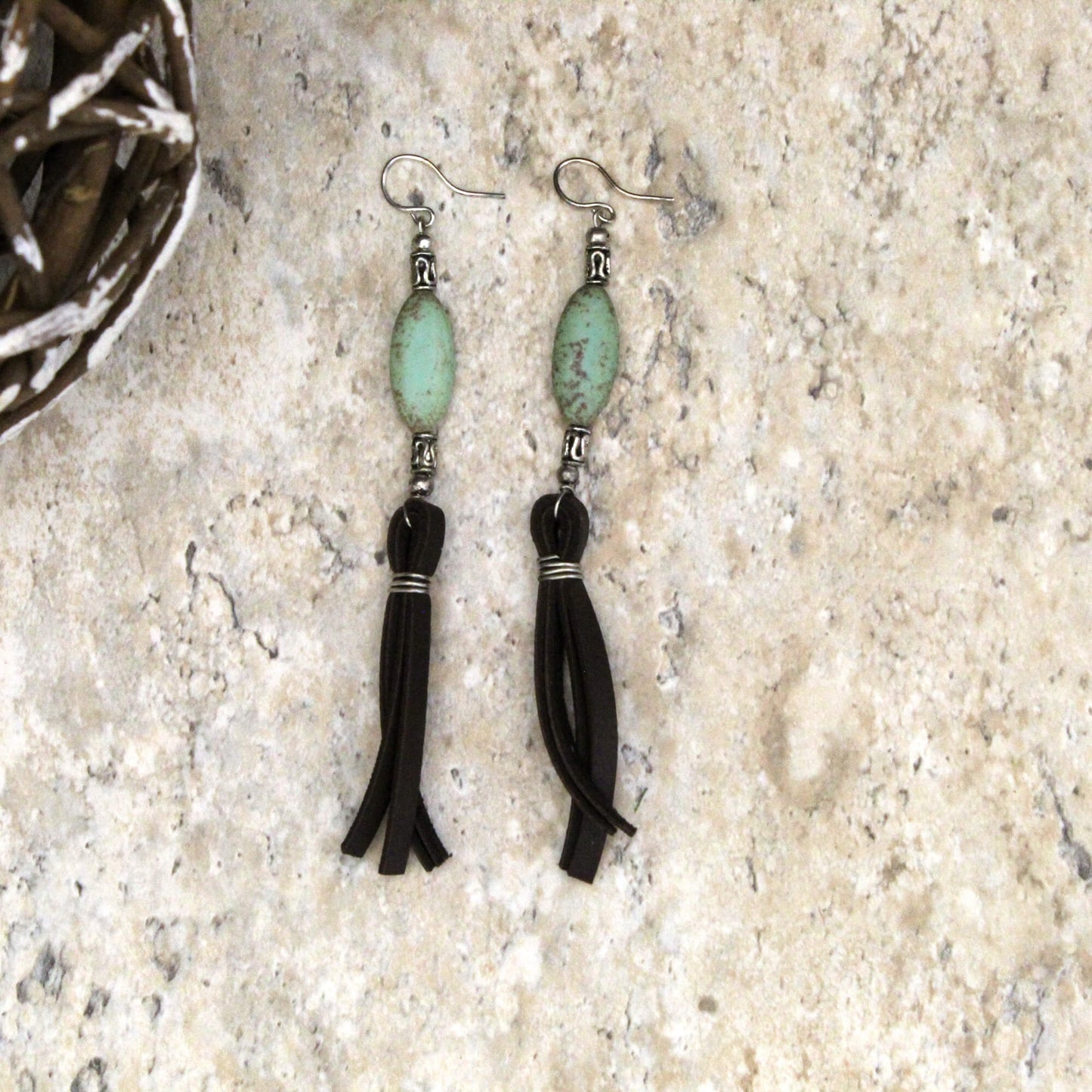 Pair of earrings with green beads and black tassels on a textured surface