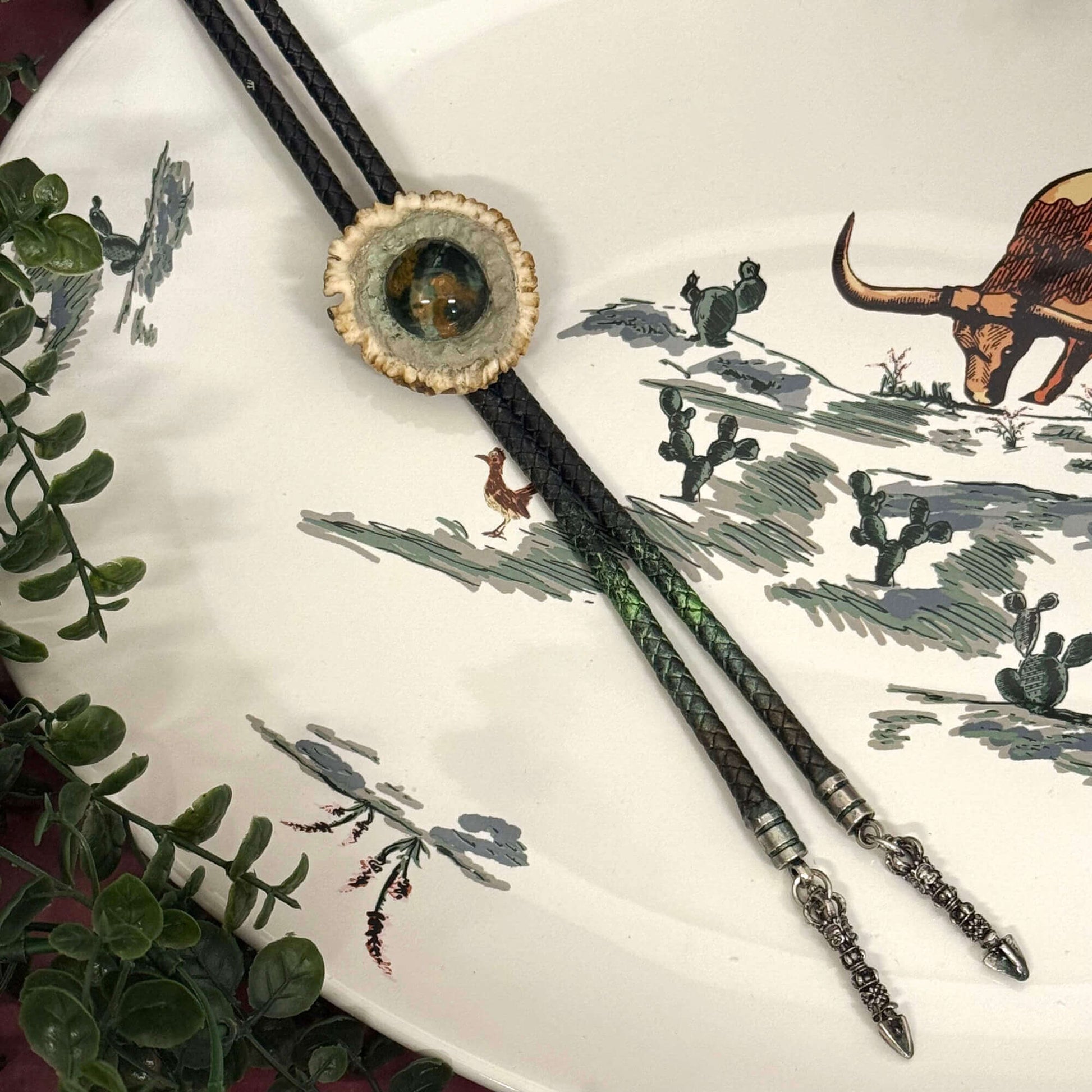 Bolo tie on a decorative plate with nature-themed design