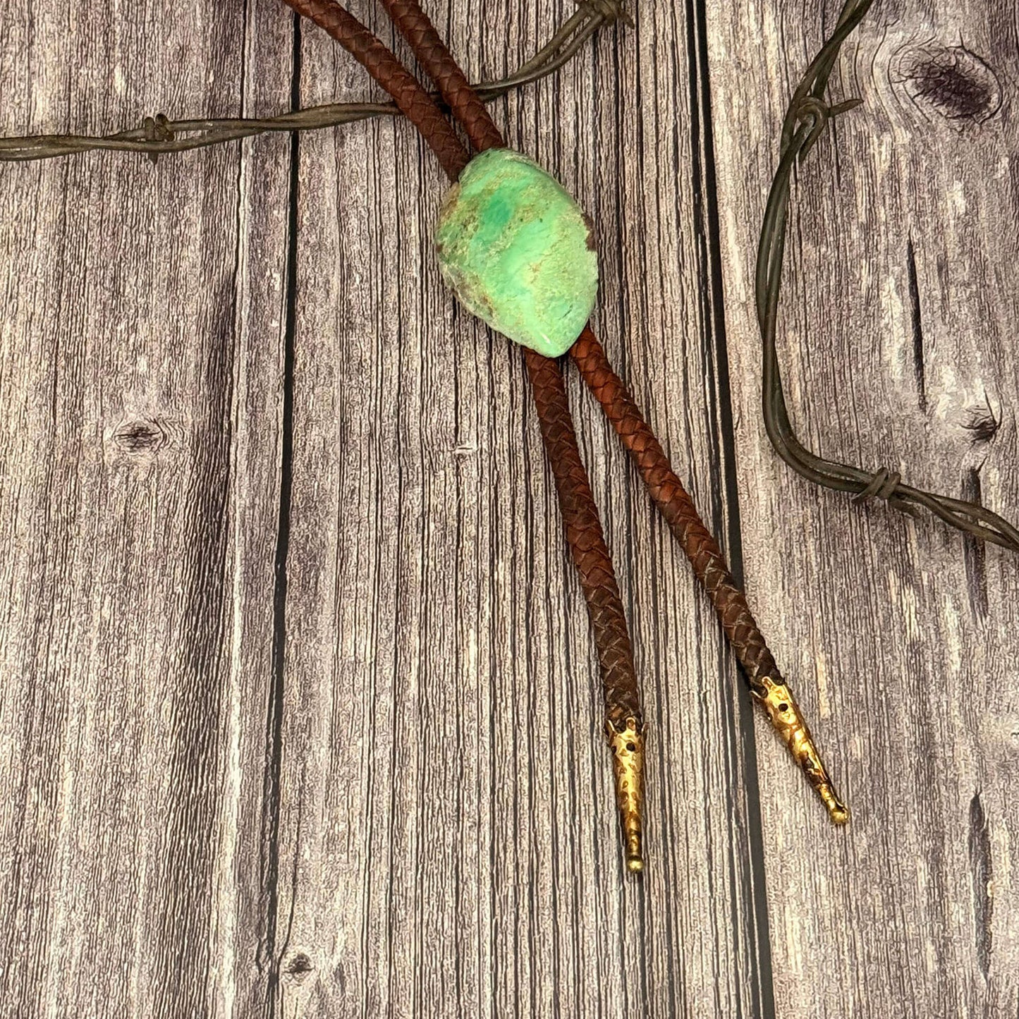 Bolo tie with green stone and gold accents on a wooden background