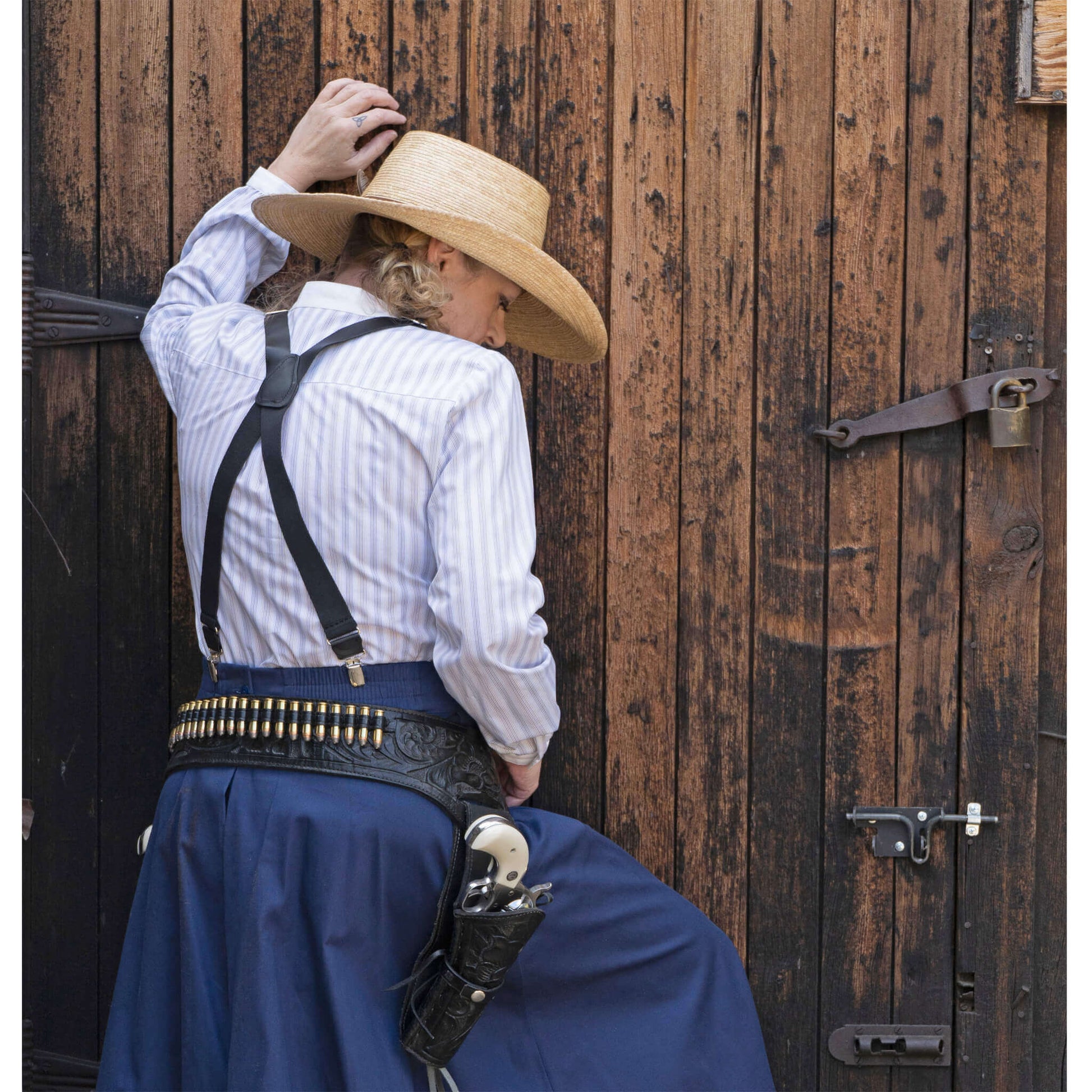 Woman in Bandit Pullover shirt and western skirt, styled with a straw hat and gun holster, against a rustic wooden background.