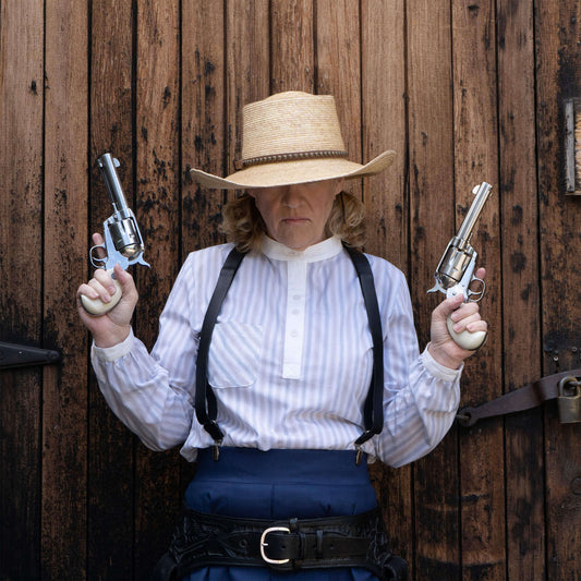 Woman in cowboy attire holding revolvers, wearing a striped Bandit Pullover Old West shirt and a straw hat.