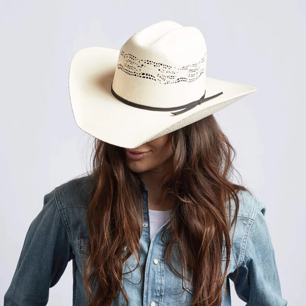Person wearing a white cowboy hat with a black band on a plain background