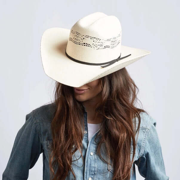 Person wearing a white cowboy hat with a black band on a plain background