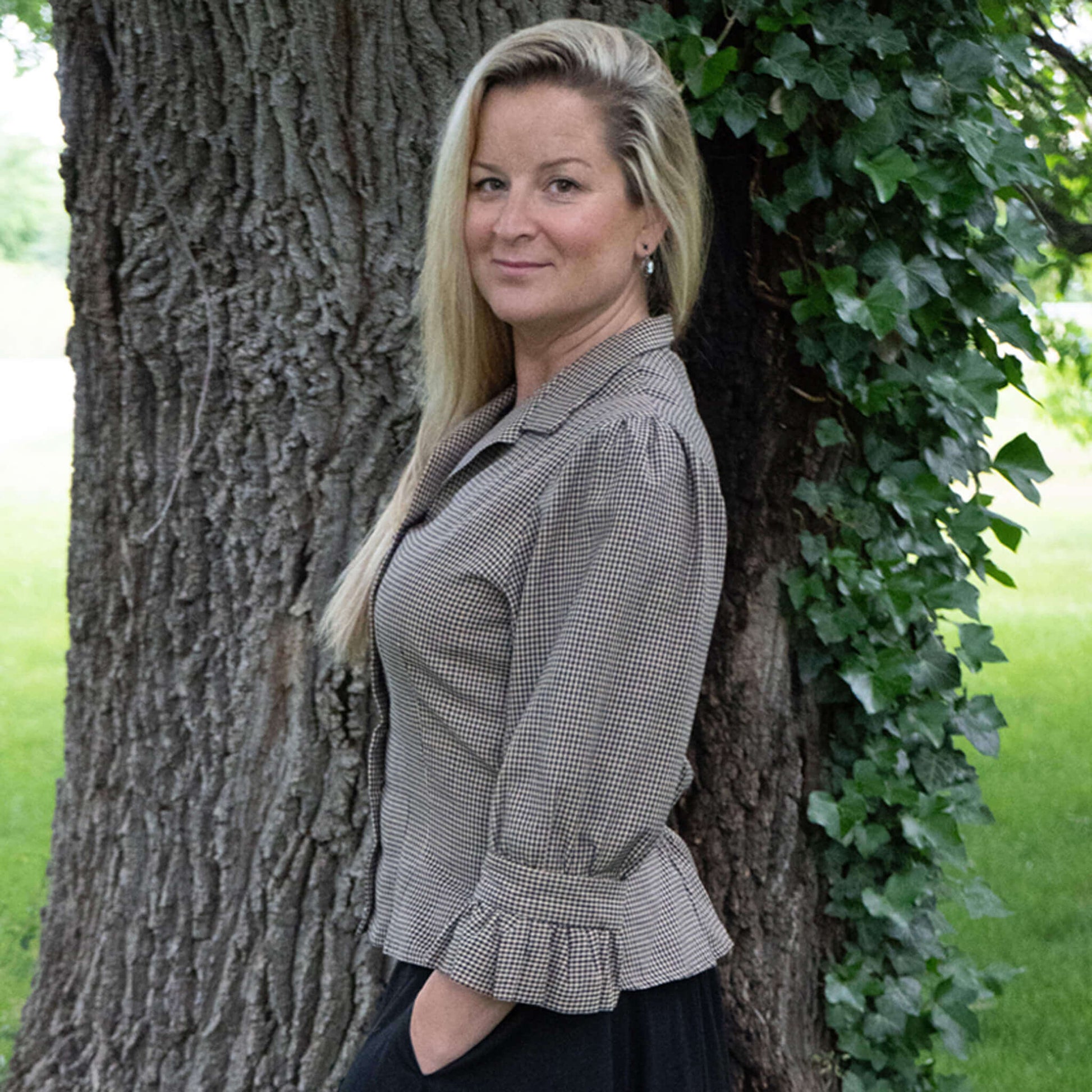 Woman modeling a Checkered Gingham Blouse with ruffled sleeves, standing against a tree.