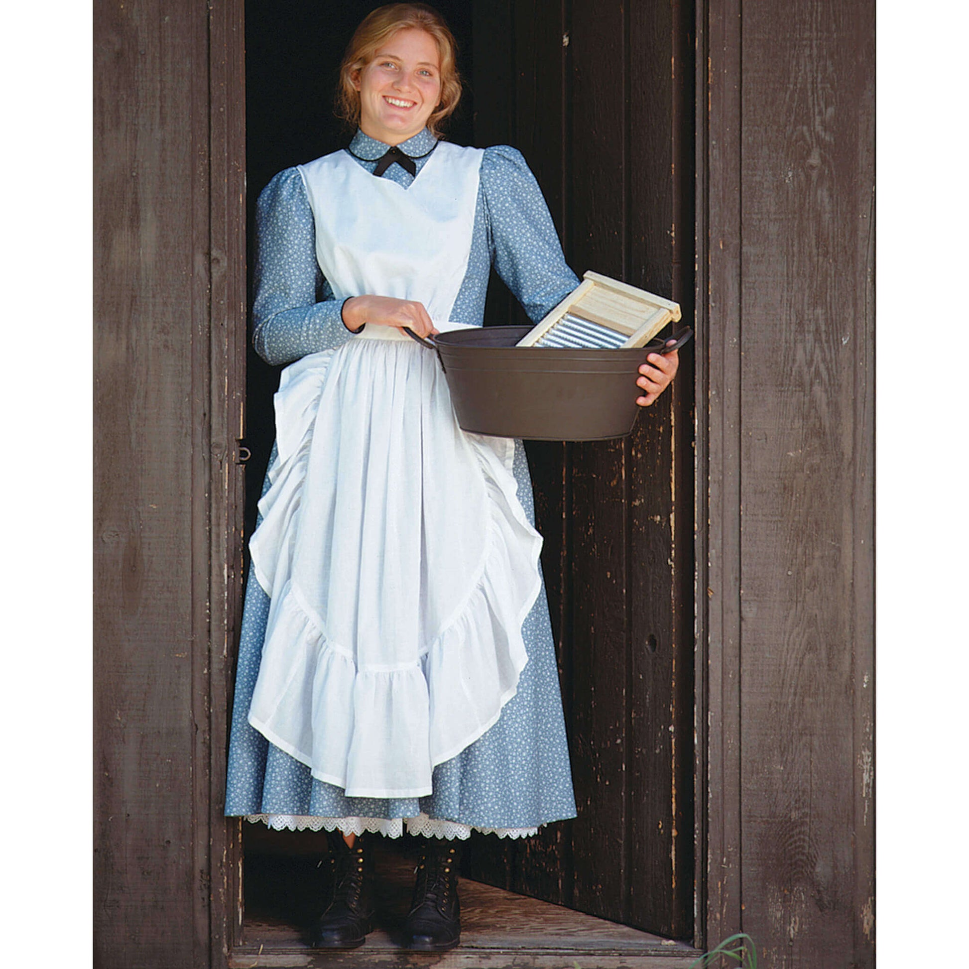 Woman in a country-style apron holding a bowl of chicken feed at a barn doorway.