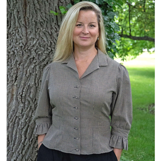 Checkered blouse with puffy sleeves on a woman standing by a tree in a green outdoor setting.