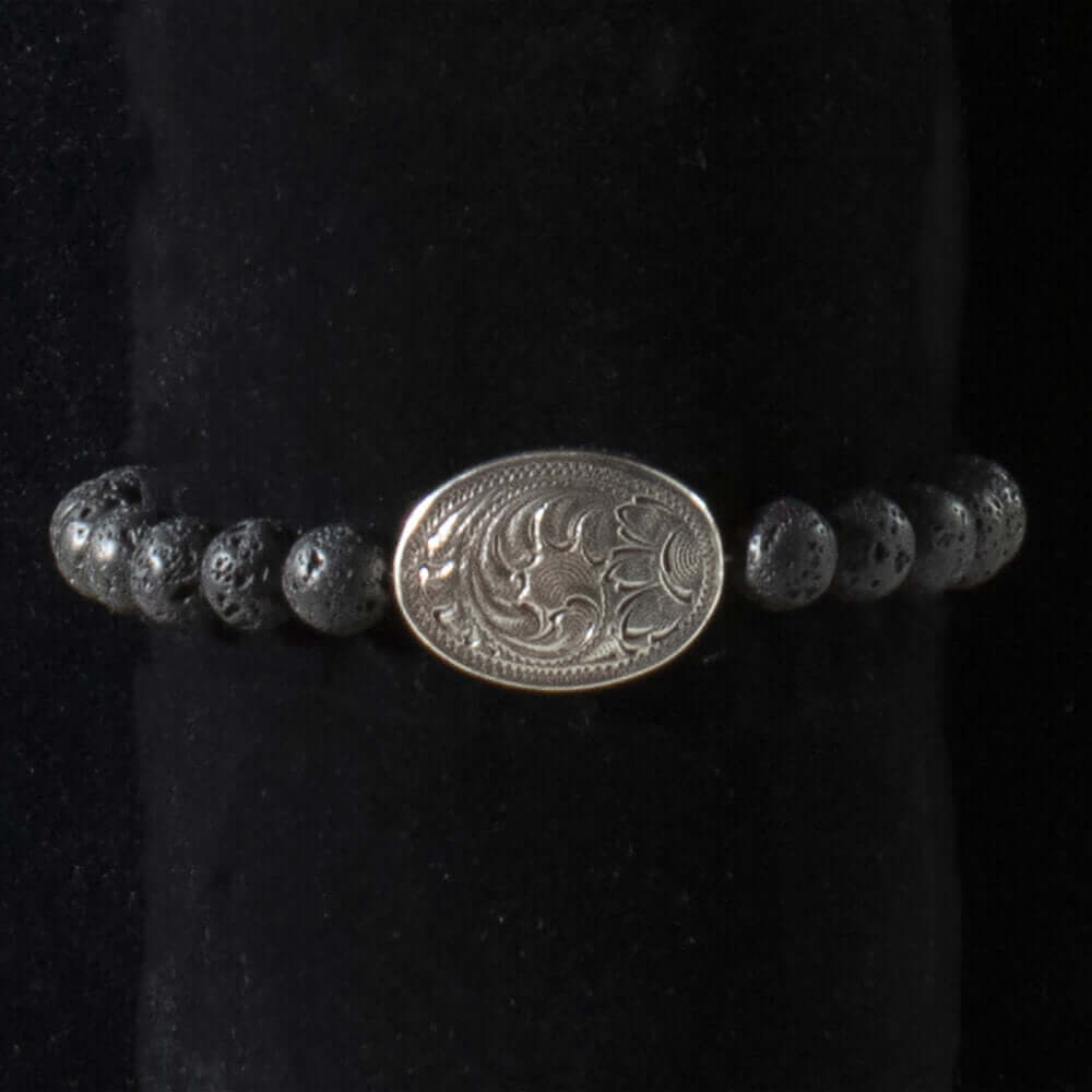 Cool cowboy style concho bracelet with lava stone beads. Hip, simple and manly stretchy pullover bracelet for cowboys or the stylish western man. Antique silver oval concho in the center that is engraved with a floral pattern.