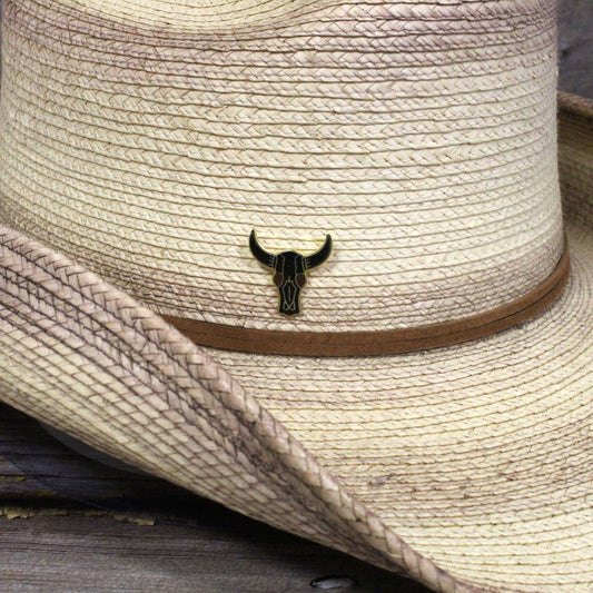 Close-up of a straw hat with a bull skull emblem on a wooden surface