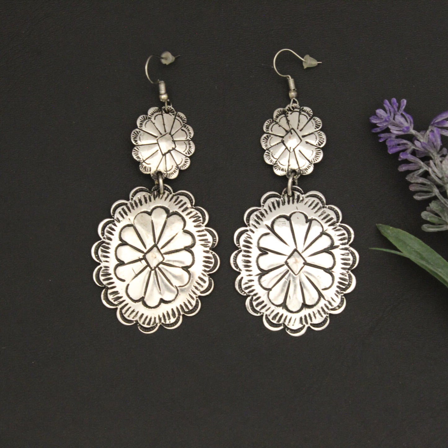 Silver floral earrings on a dark background with lavender flowers.