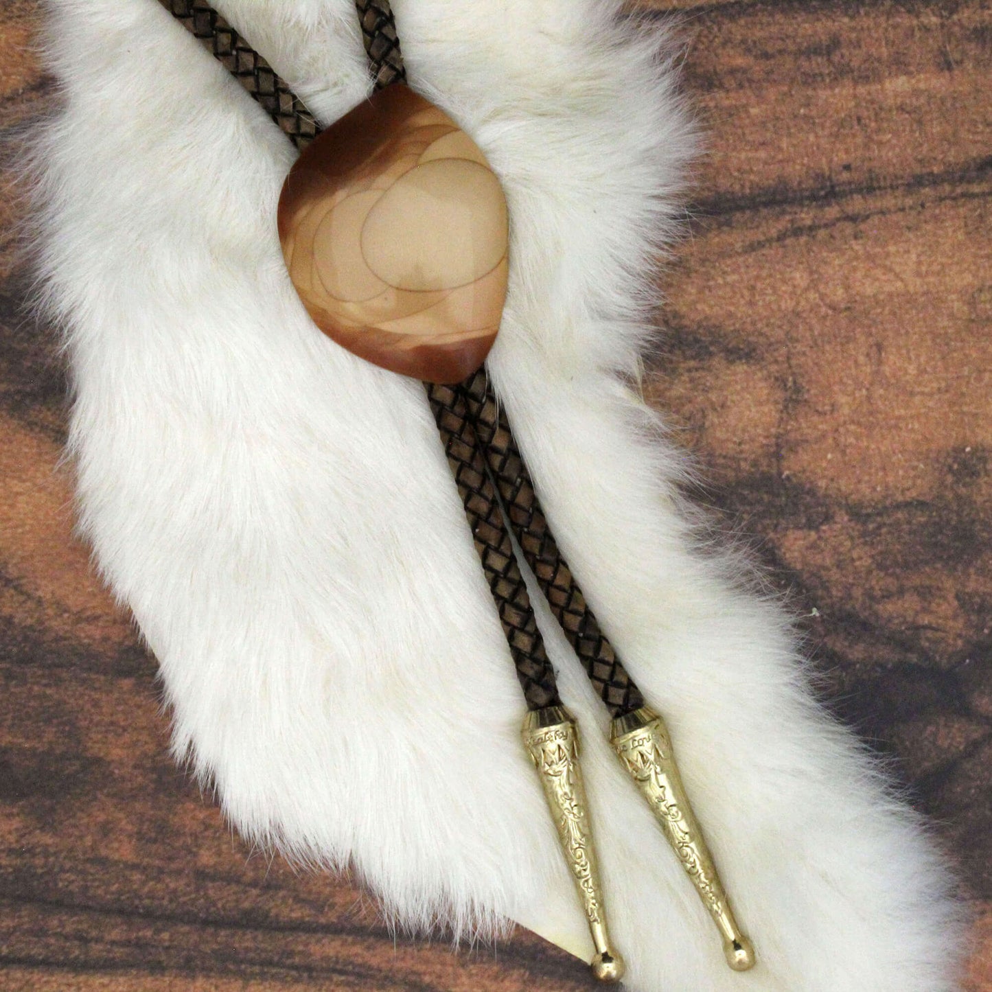Bolo tie with wooden center and gold tips on a white fur background