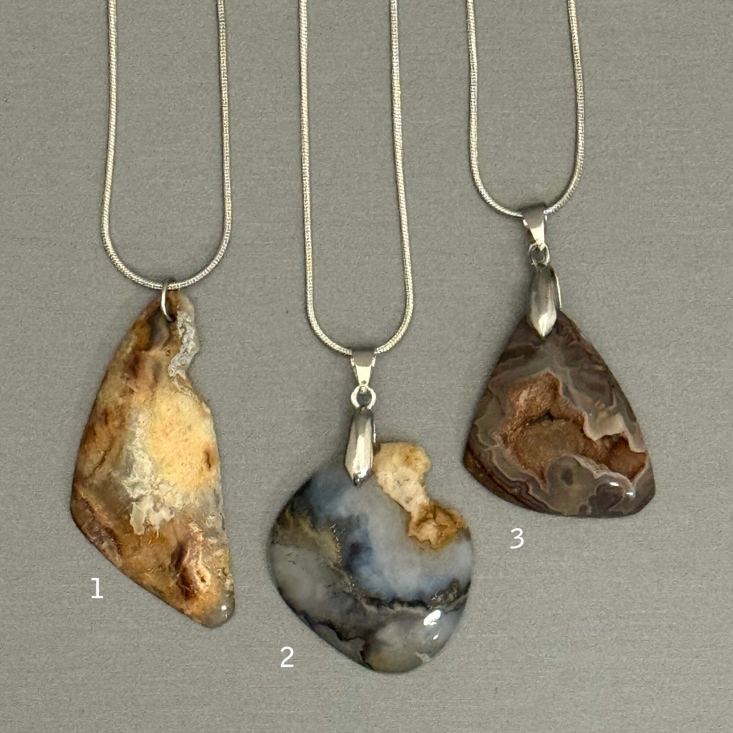 Three agate pendants on silver necklaces against a gray background