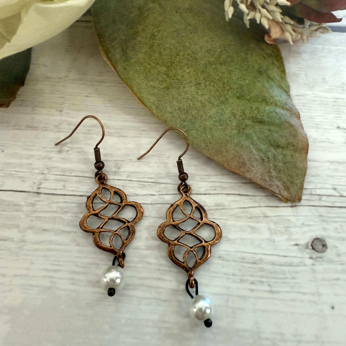 Bronze earrings with pearl drops on a wooden surface with leaves in the background