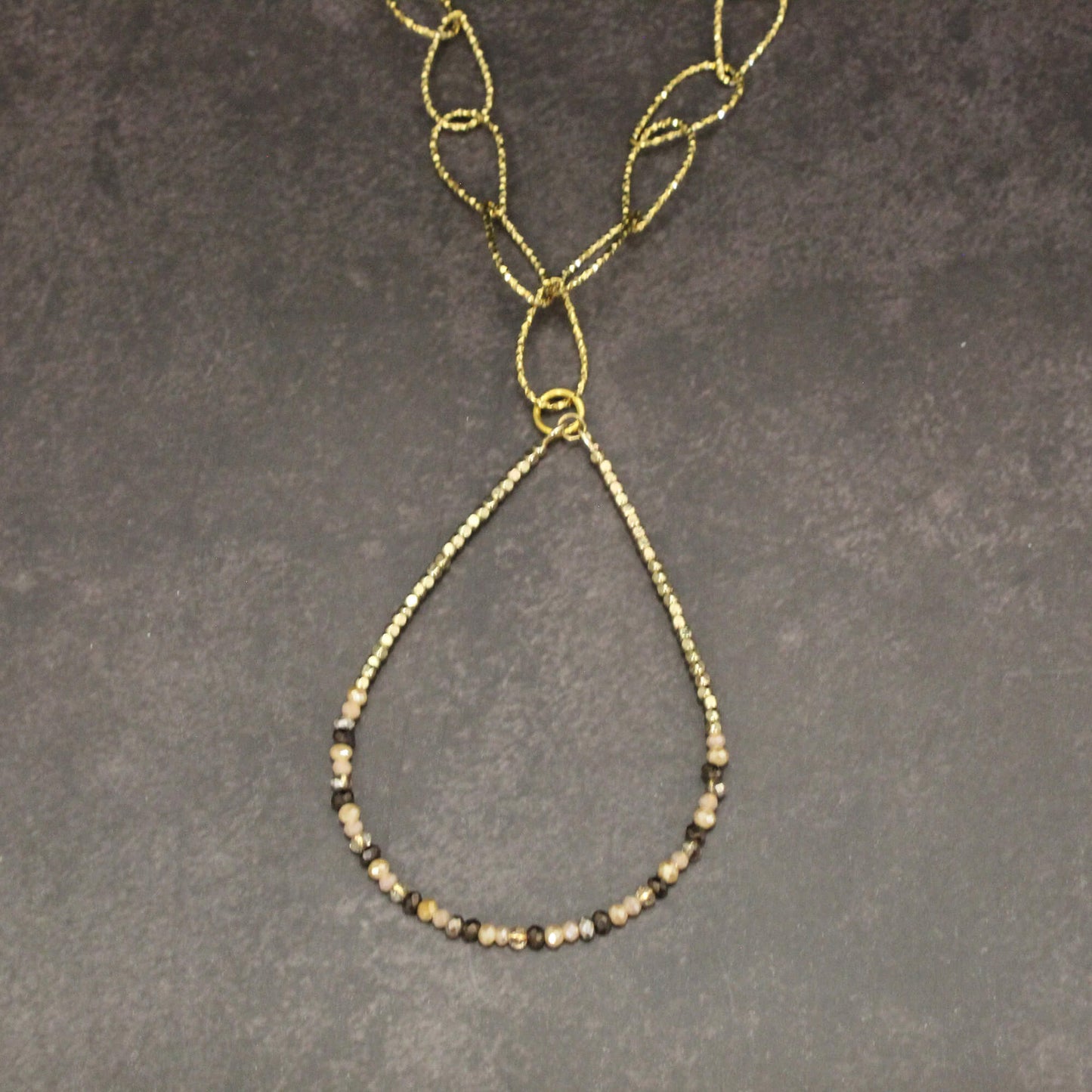 Gold necklace with beaded chain on a gray background