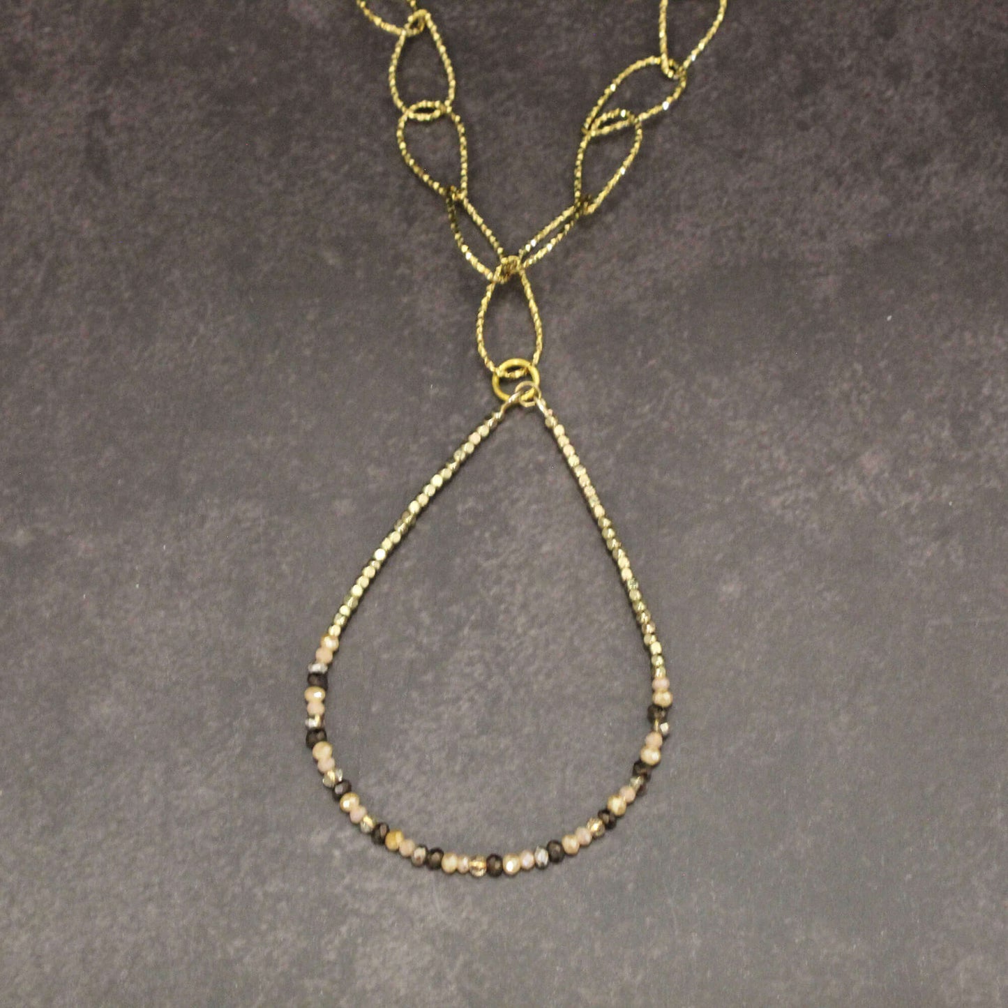 Gold necklace with beaded chain on a gray background