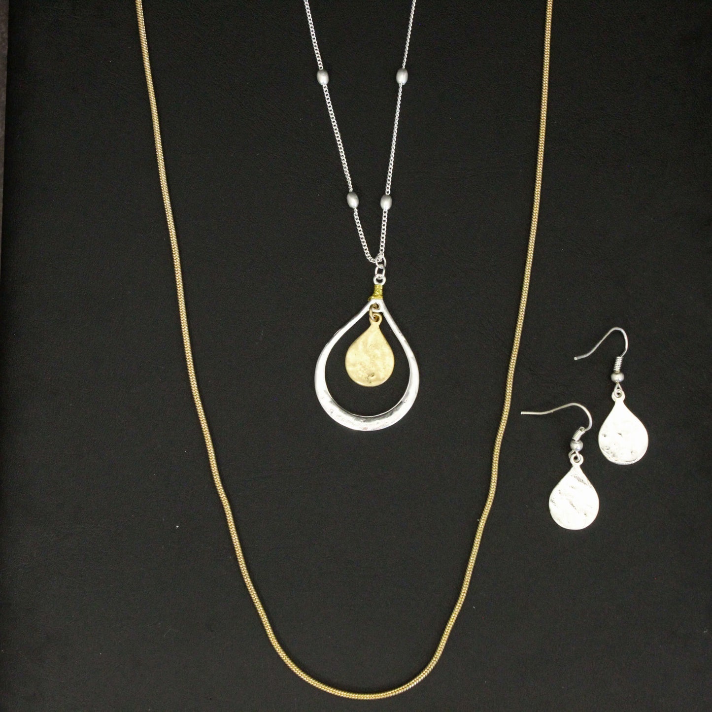 Gold necklace with a teardrop pendant and matching earrings on a black background