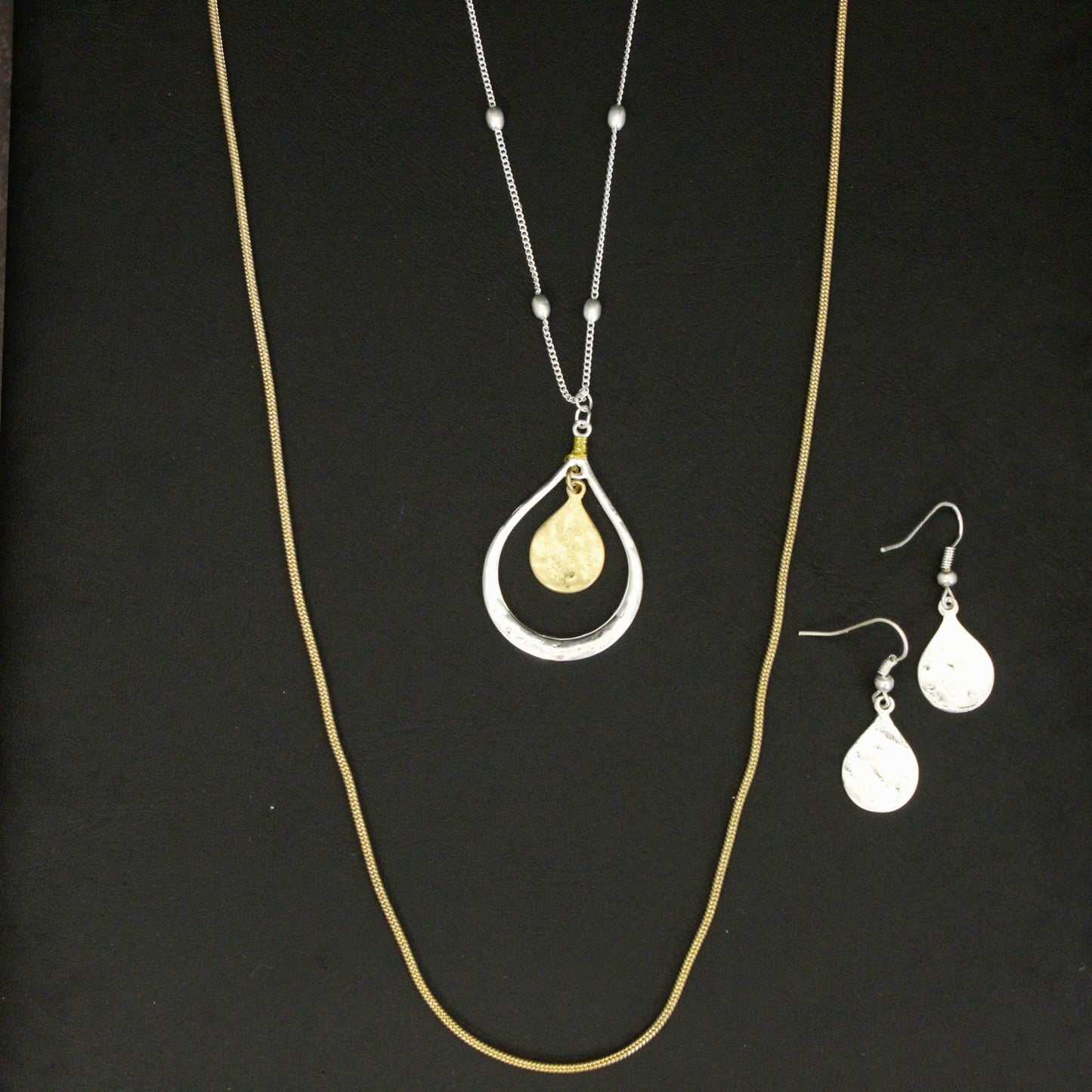 Gold necklace with a teardrop pendant and matching earrings on a black background
