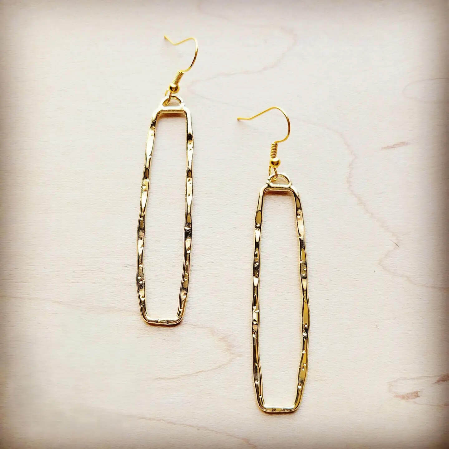 Gold dangle rectangle earrings on a beige marble background