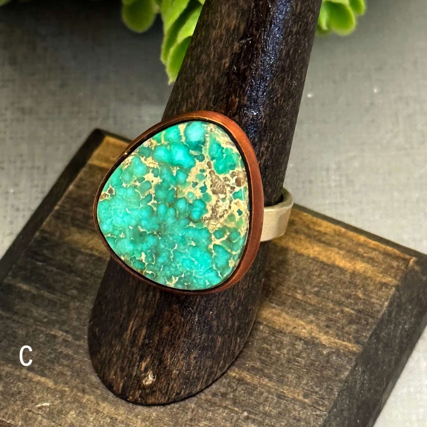 J Marie genuine turquoise ring with a unique triangular stone set on an adjustable band, displayed on a wooden stand.