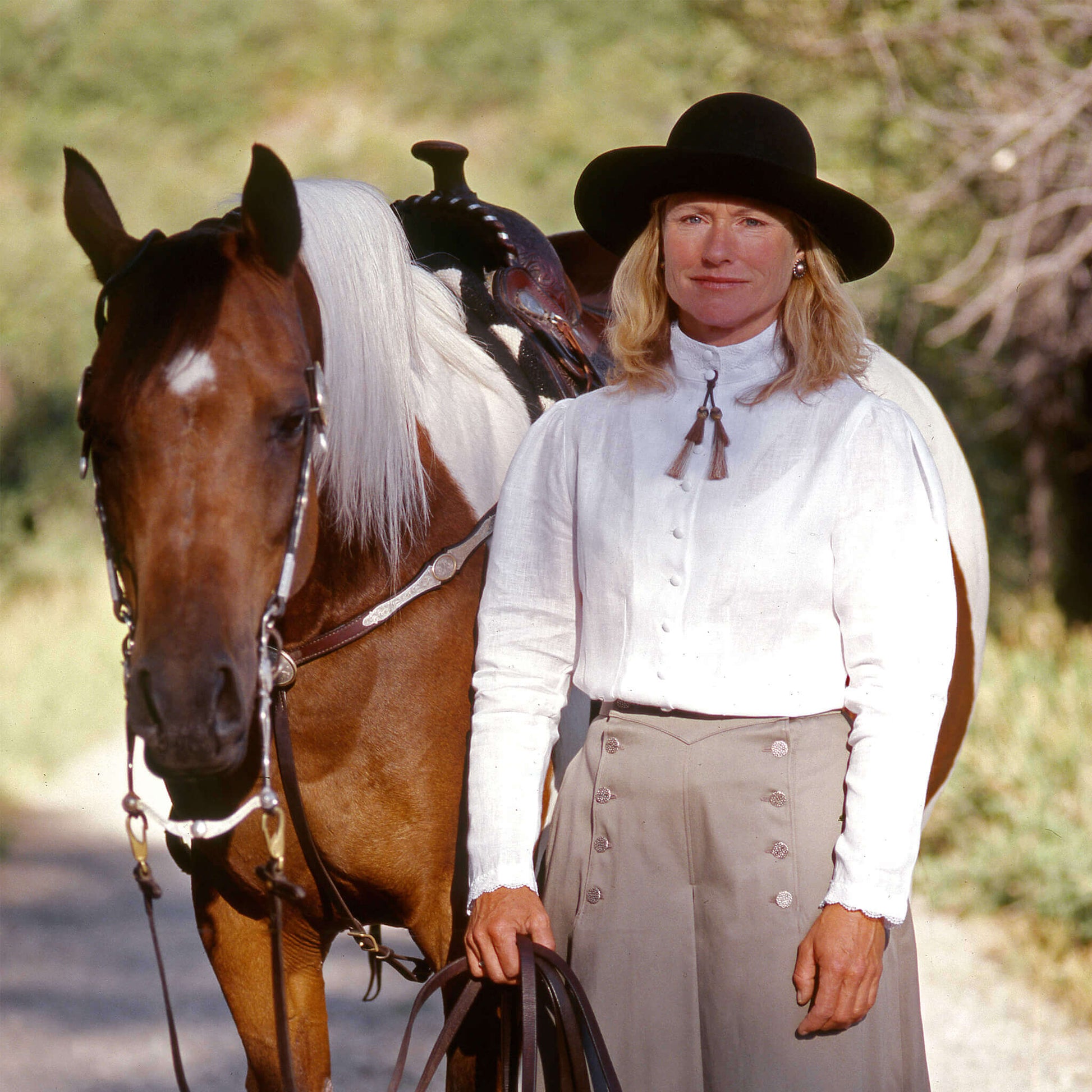 Woman in white Nell Blouse standing beside a horse, showcasing elegant 1800's western style fashion.