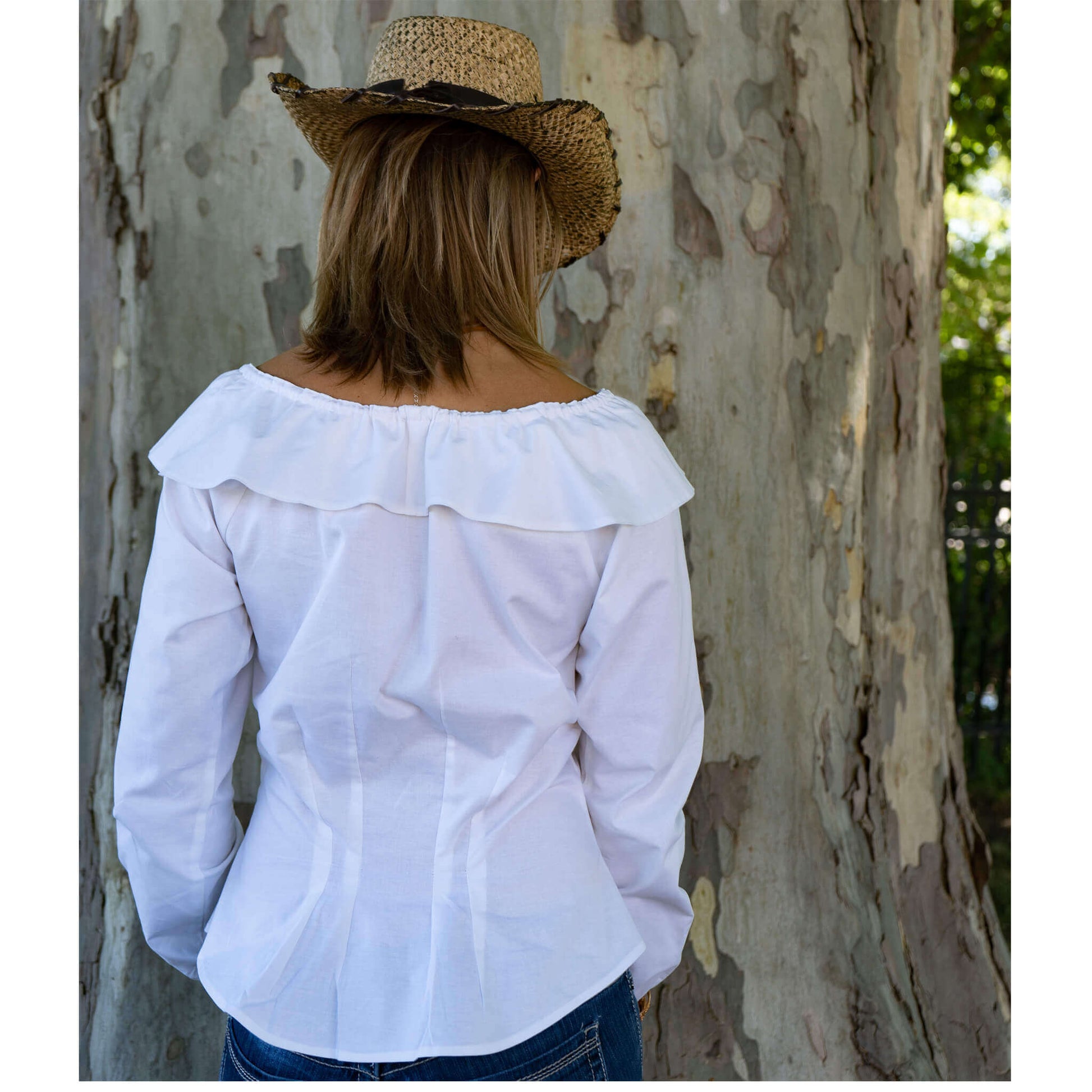 Back view of a woman in a white off-shoulder ruffle blouse, wearing a straw cowboy hat against a tree backdrop.