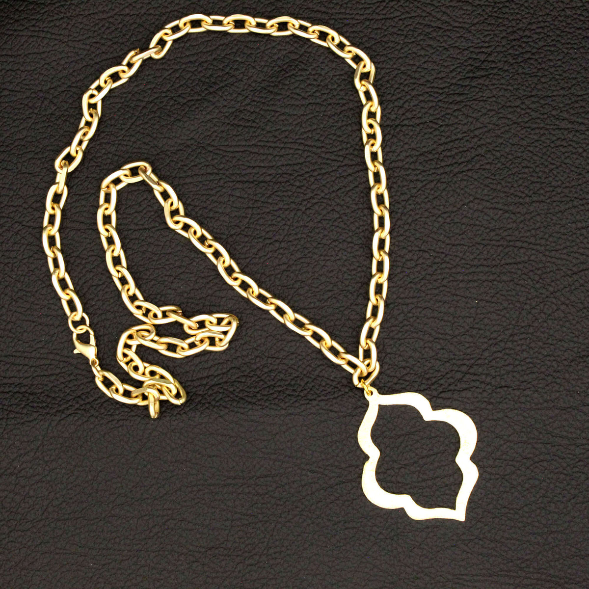 A gold chain necklace with a white cloud-shaped pendant, displayed on a textured black background.