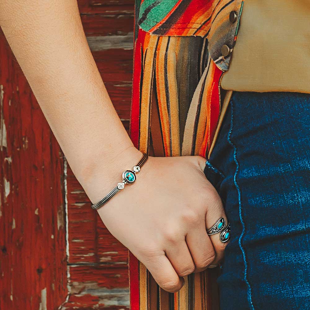 Close-up of a hand wearing a Turquoise Cuff Bracelet, showcasing copper and cubic zirconia stones against a colorful backdrop.
