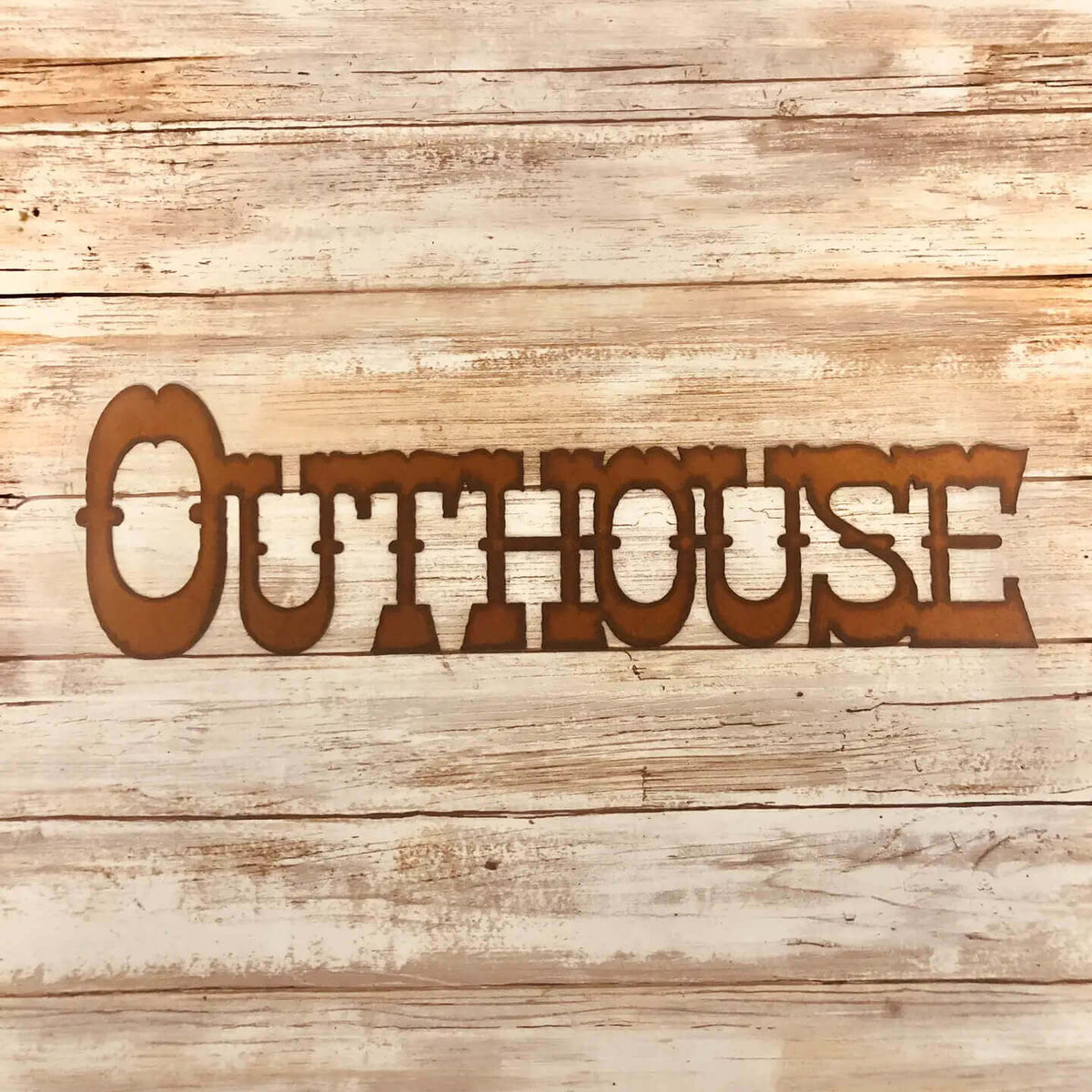 A laser-cut metal wall sign spelling 'OUTHOUSE' in a rustic brown color, displayed against a light-colored, weathered wood plank background.