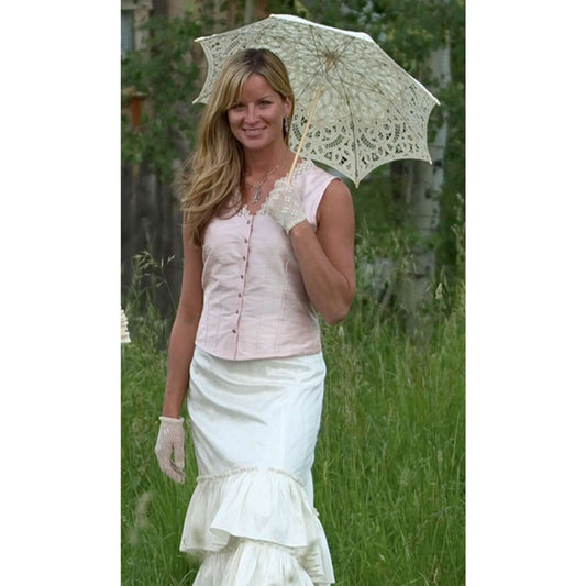 Elegant woman in a pink silk corset cover camisole with lace detail, holding a decorative parasol in a grassy setting.