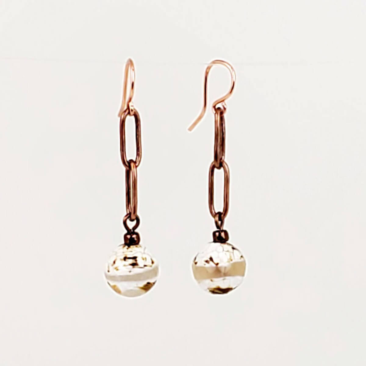 A pair of rose gold drop earrings featuring elongated paperclip chain links and faceted clear glass beads, shown against a plain off-white background.