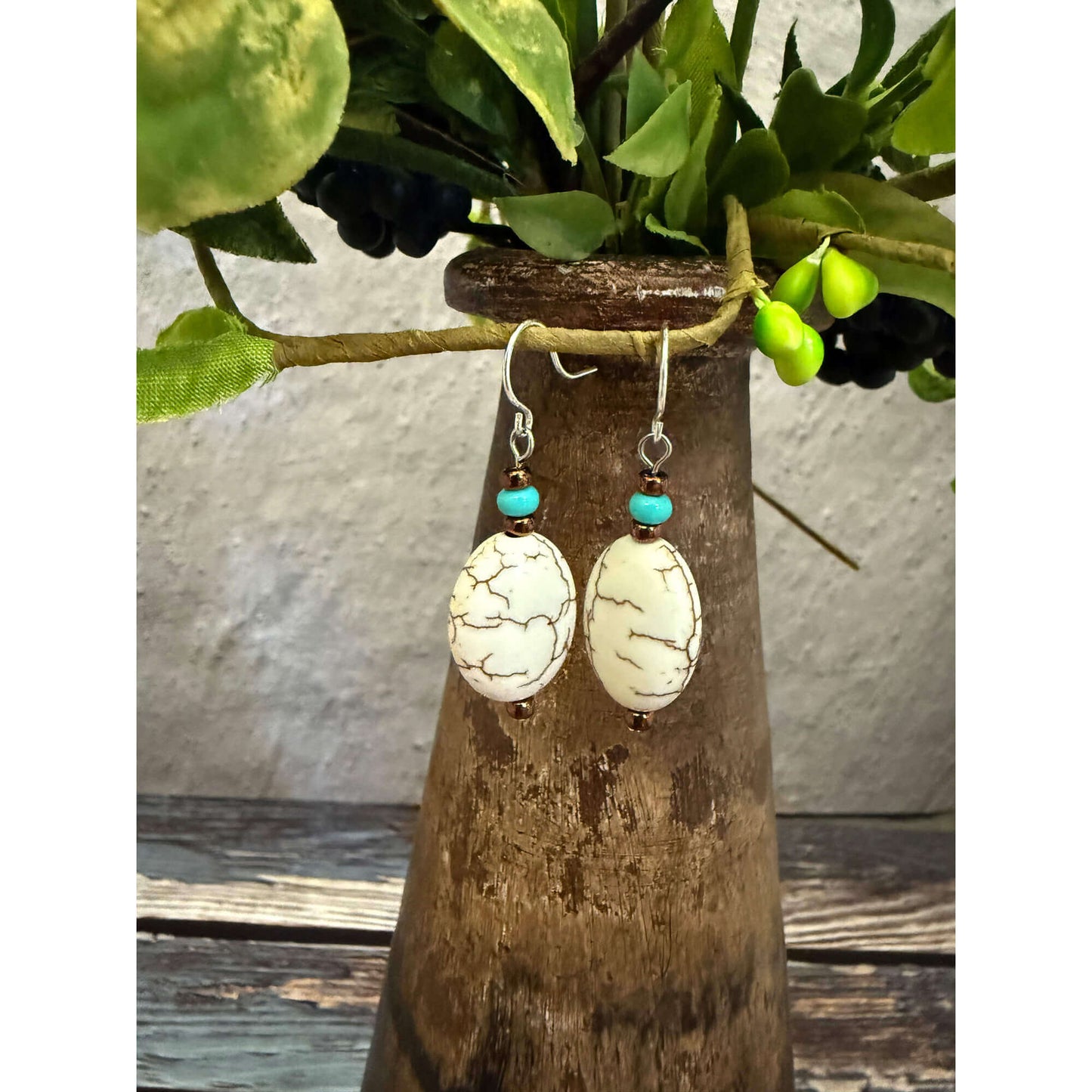 Pair of earrings with white and turquoise stones hanging on a branch.
