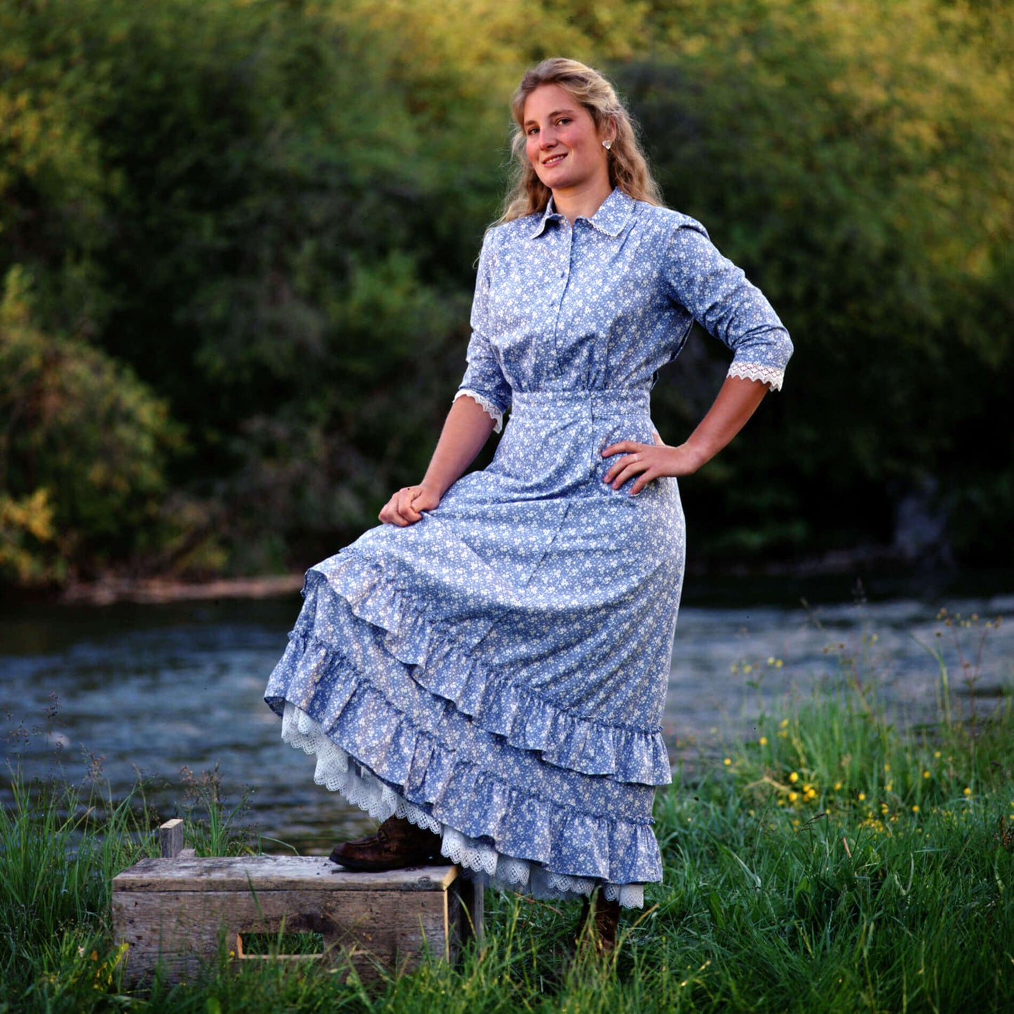 Model wearing Prairie Schooner Authentic Ladies Dress in periwinkle calico by Cattle Kate, showcasing vintage style and ruffles.