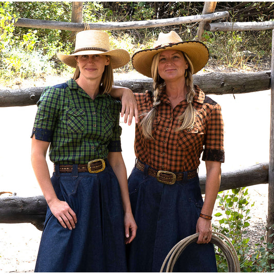 Two women wearing Rodeo Round-Up Ladies Shirts in a western setting, showcasing stylish plaid designs and cowboy hats.