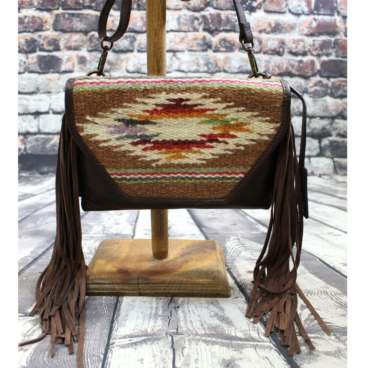 Ariat Sheridan crossbody bag is genuine leather and God’s eye southwestern pattern on handwoven fabric on the front flap. Brown suede fringe on the sides. Snap closure with one zipper pocket inside. Measures: 9” X 7” X 1”. Imported.