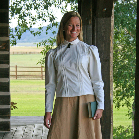 Model wearing a Schoolmarm Country Blouse with puffed sleeves and a black silk tie outdoors.