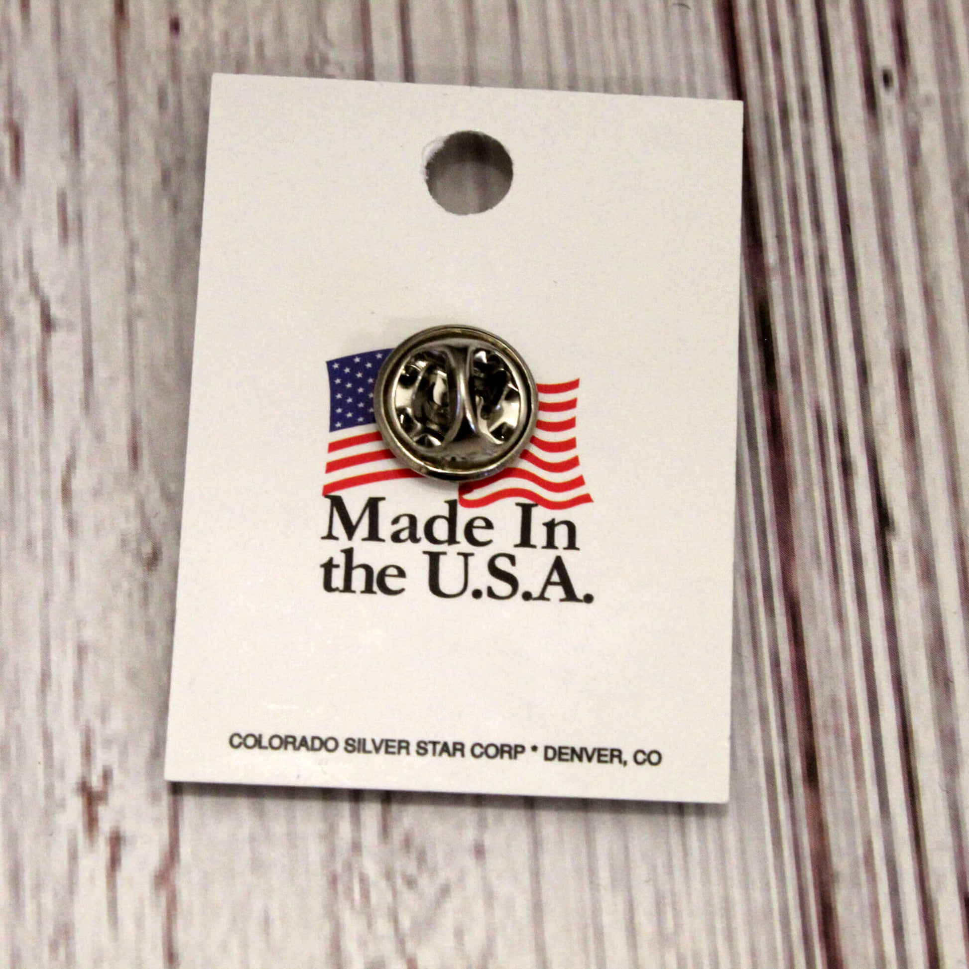 Pin with American flag design on a 'Made in the U.S.A.' card, on a wooden surface.