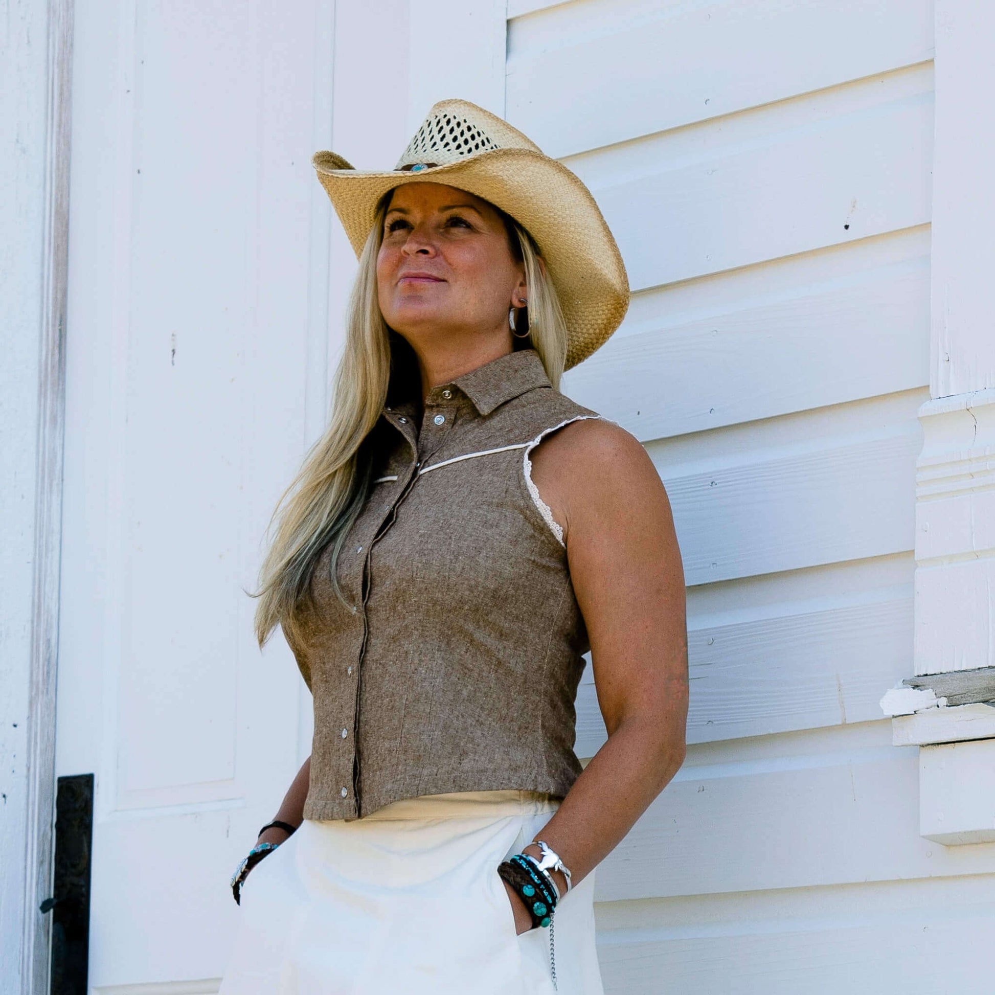 Woman wearing Sierra Rodeo Cowgirl Blouse and cowboy hat against a rustic white backdrop.