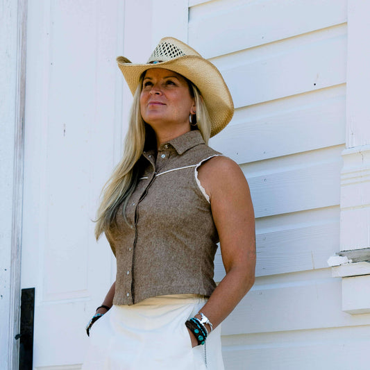Woman wearing Sierra Rodeo Cowgirl Blouse and cowboy hat against a rustic white backdrop.