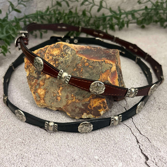 Leather belt with metal conchos on a stone surface with greenery in the background