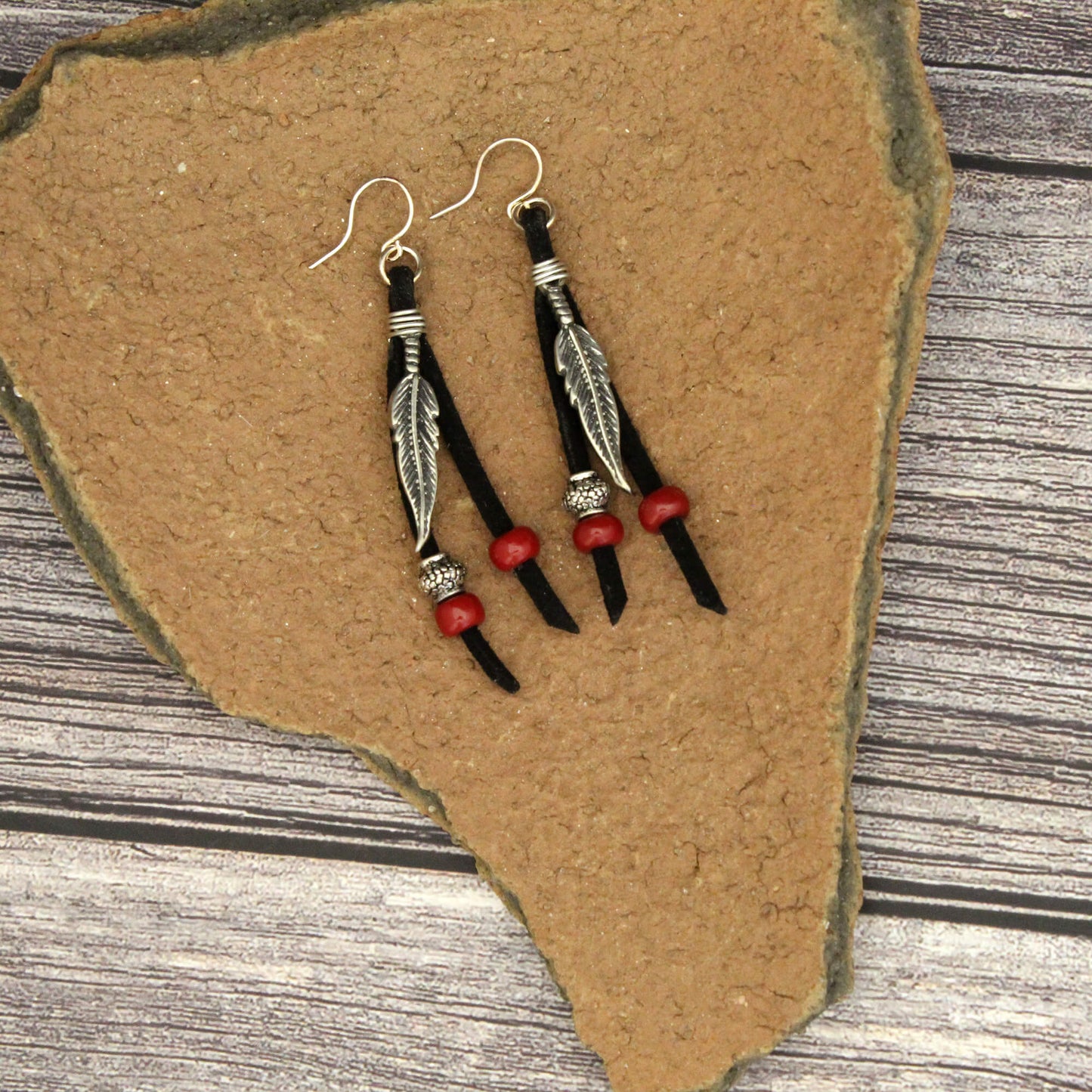 Pair of feather-themed earrings with red beads on a stone surface