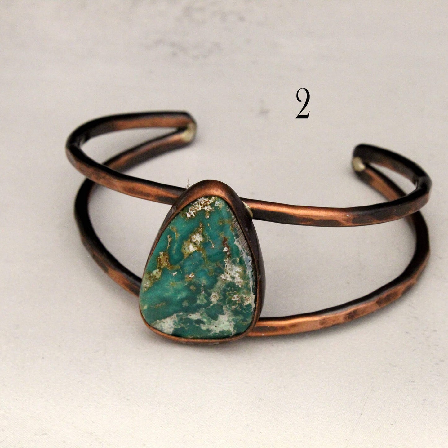 Copper bracelet with a green stone on a light gray background