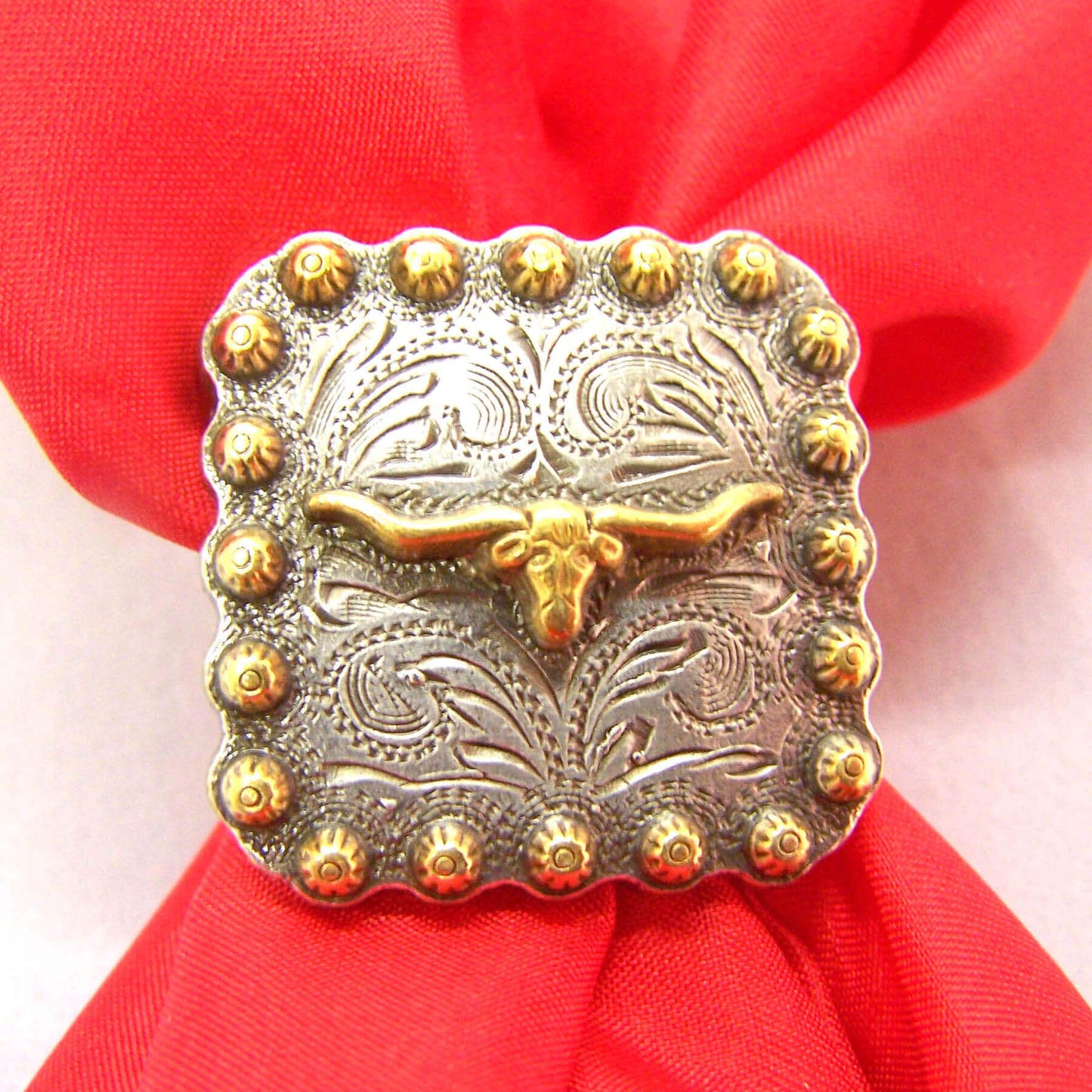 Secure your wild rag with a Cattle Kate Scarf Slide. This design features a brass longhorn centered on a solid square nickle base. A etched design as a background and bordered with brass studs this slide is sure to last.