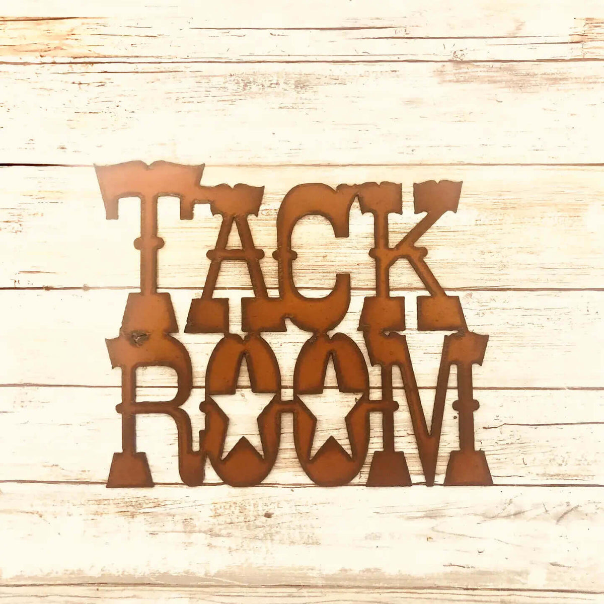 Copper-colored metal wall art spelling 'TACK ROOM' in a rustic western-style font, displayed on a light wood plank background.