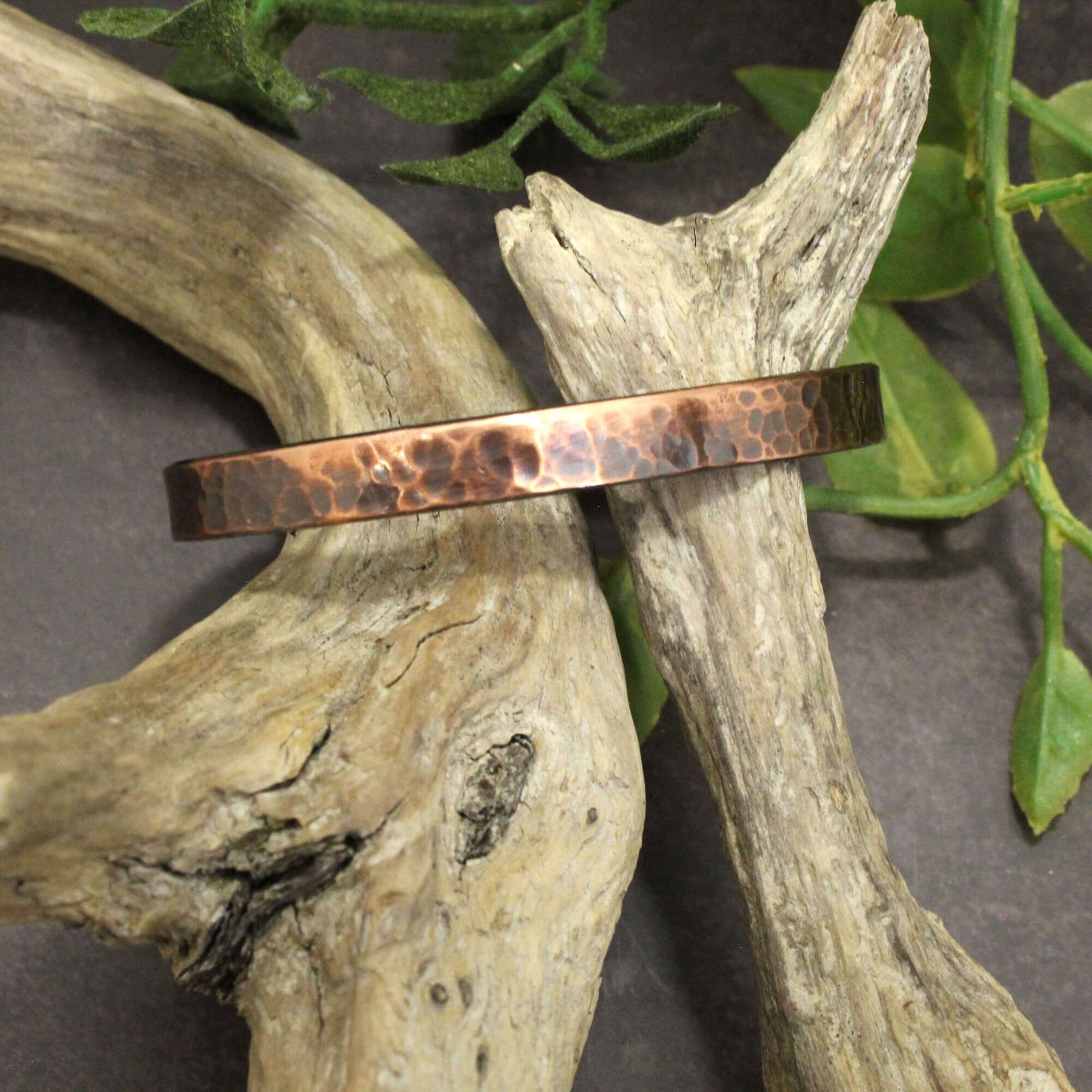 Copper bracelet on a piece of driftwood with green leaves in the background