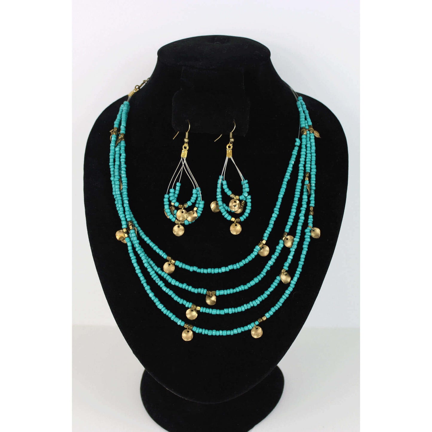 Nothing quite sets off the color of turquoise than gold. This four-strand Mag Turquoise beaded necklace is accented by petite antiqued brass coins and gold tone squared beads. Strands are tiered for an added regal effect. Necklace measures 21″ with extension chain and lobster claw clasp. Matching hoop earrings on hypoallergenic ear wires