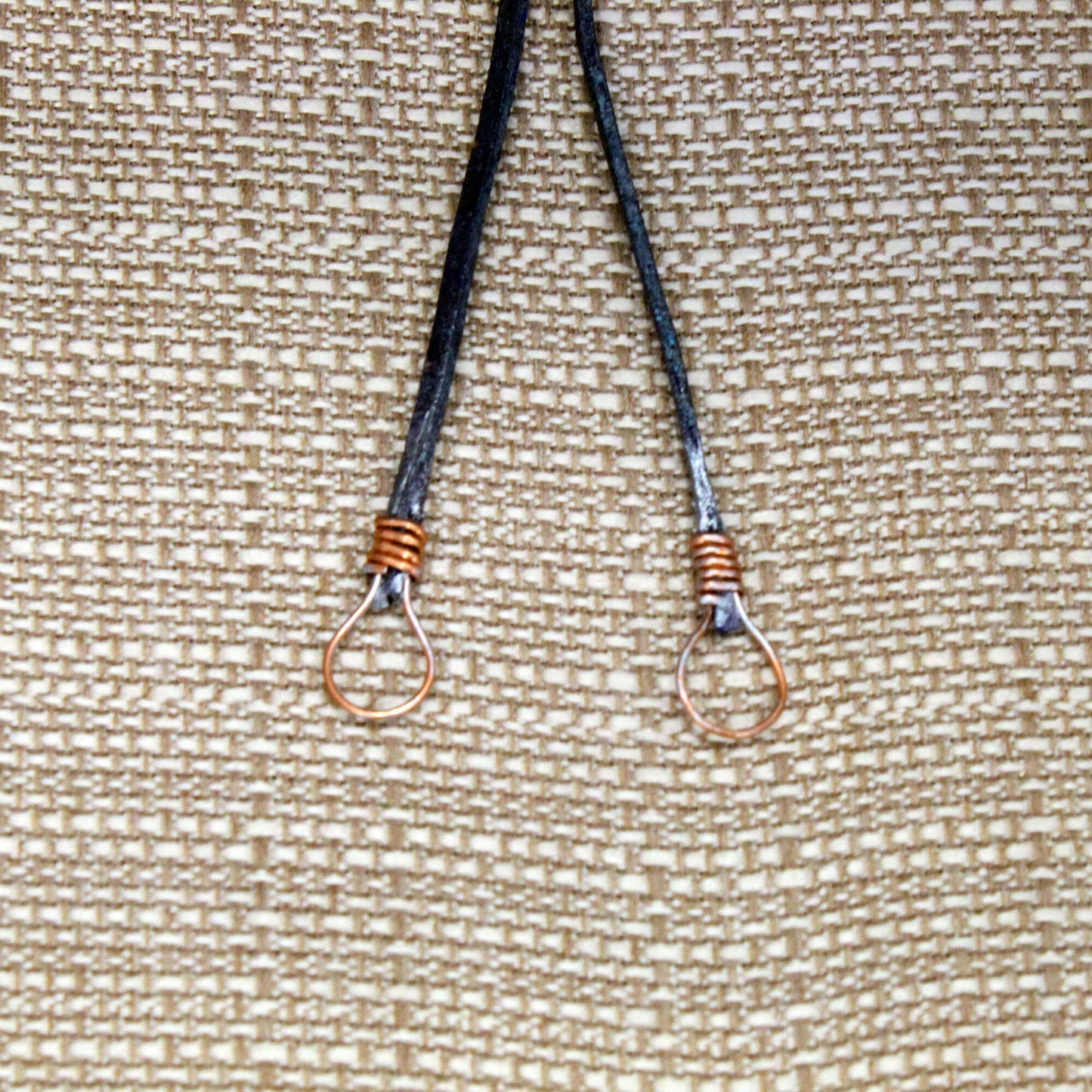 Two black lanyards with metal hooks on a textured beige background