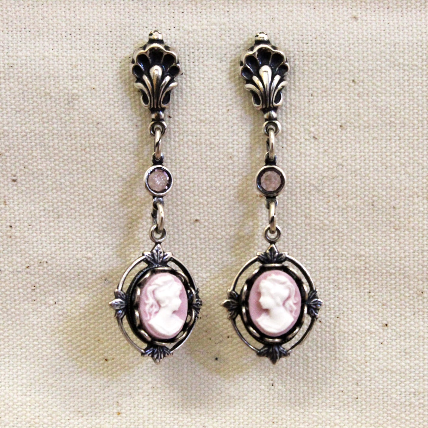 Pair of silver earrings with pink cameo stones on a beige fabric background