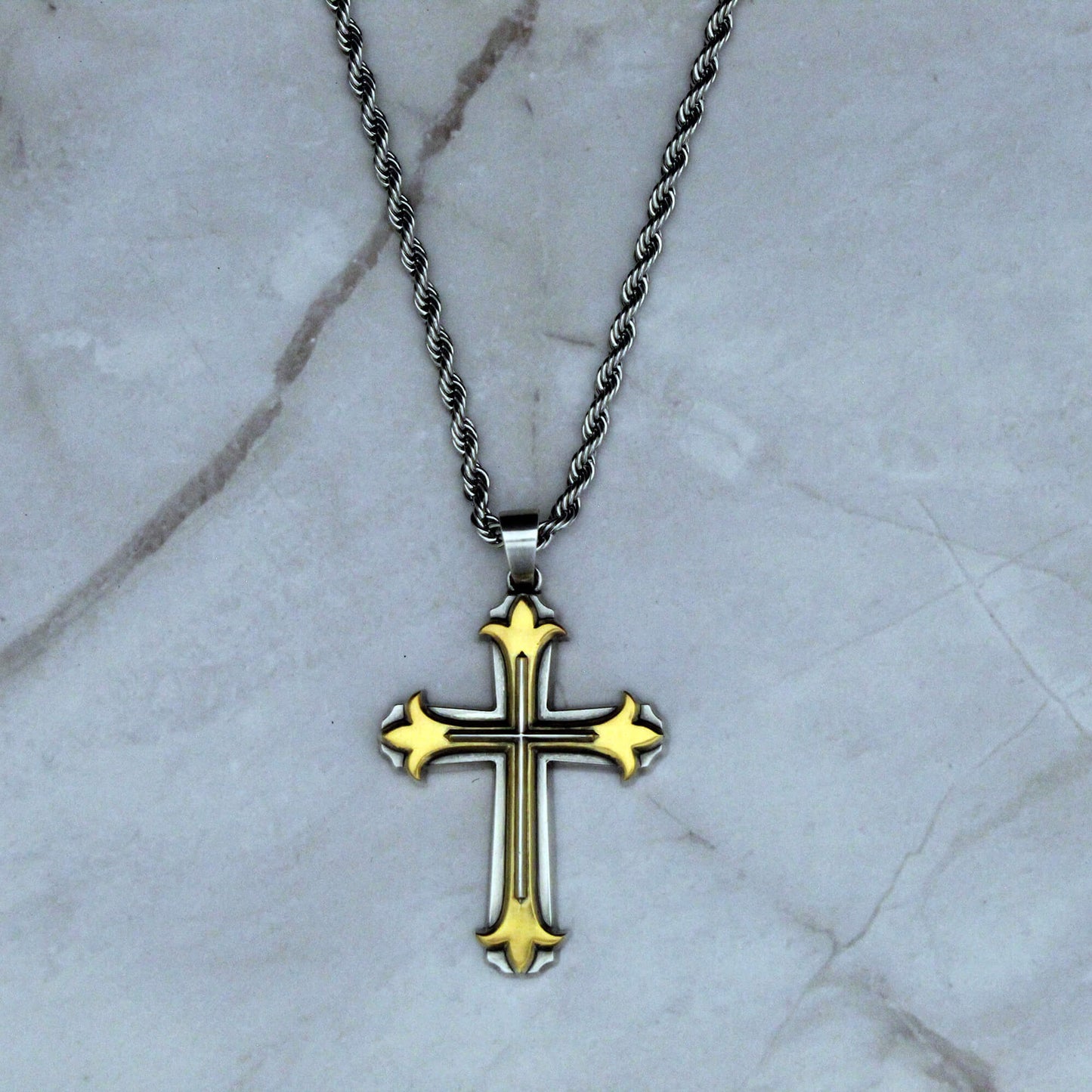 Gold cross pendant on a silver chain against a marble background