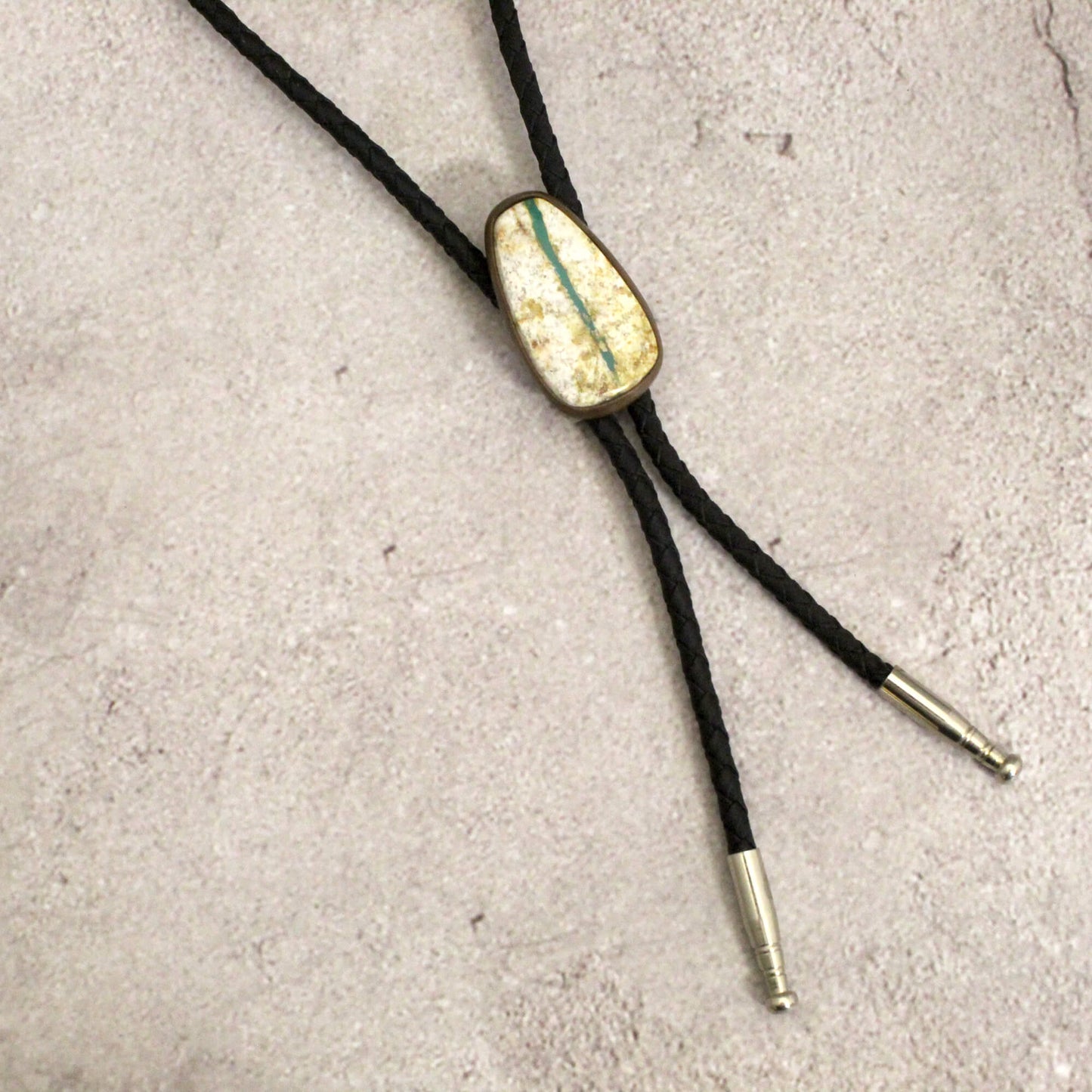 Bolo tie with gold and green stone on a concrete surface